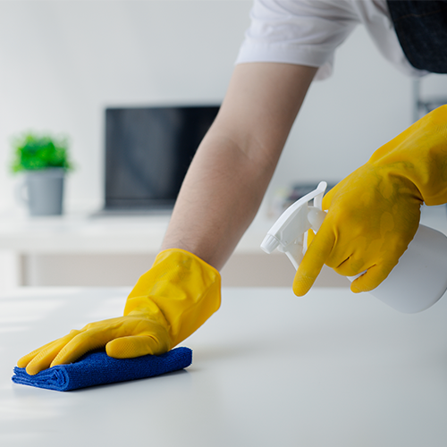 personne avec des gants jaunes nettoyant et désinfectant un plan de travail.